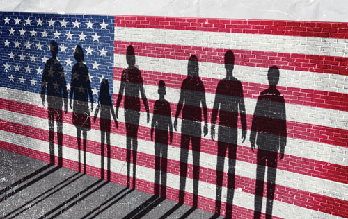 Silhouettes of people stand before an American flag painted on a brick wall