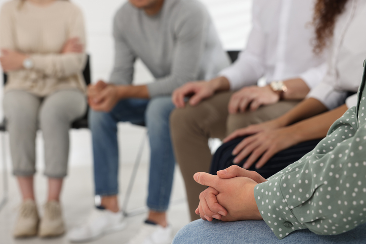 People sitting in a circle during a group discussion, with one participant’s clasped hands in the foreground