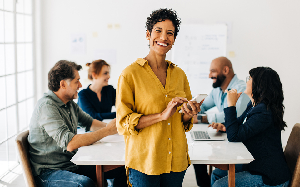 woman smiling while she sits at a conference table with colleagues 